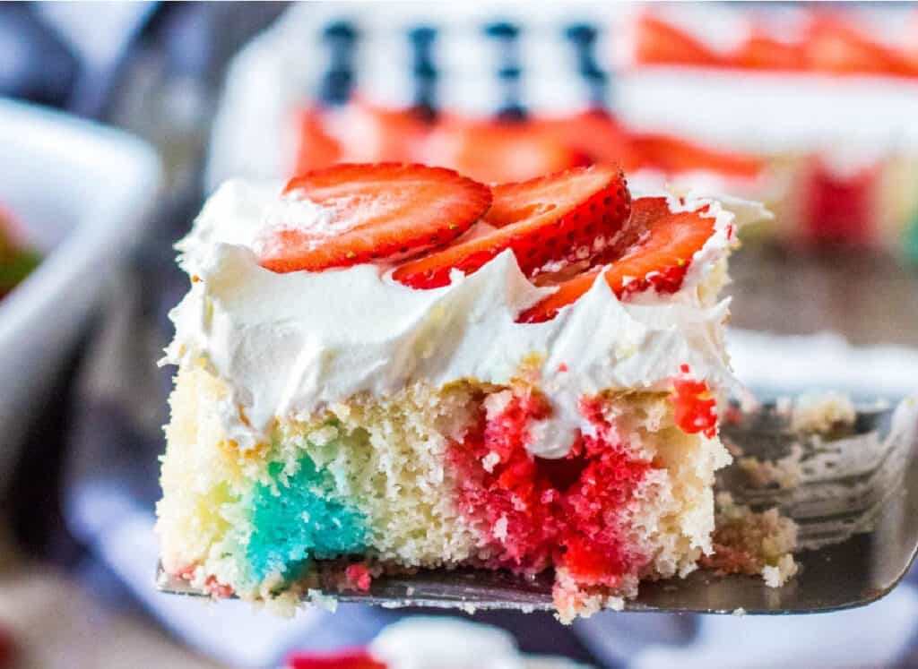 Piece of cake with red and blue koolaid dye, topped with whipped cream and sliced strawberries.