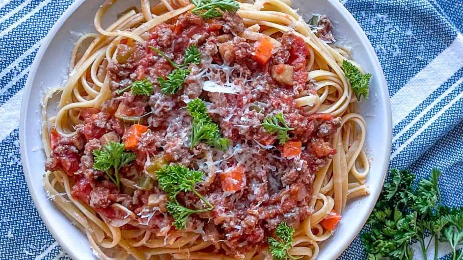 linguine bolognese on a white plate topped with parsley and parmesan.
