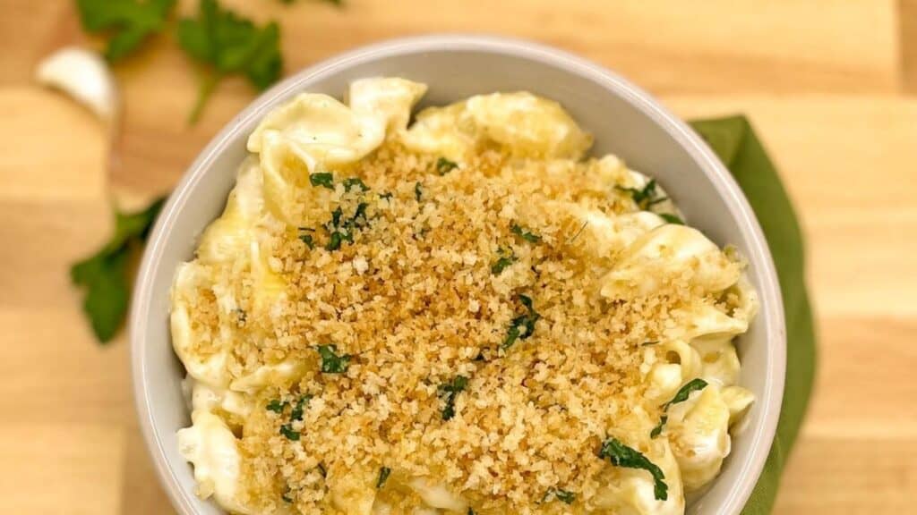Mozzarella and white cheddar mac and cheese in a white bowl topped with breadcrumbs.