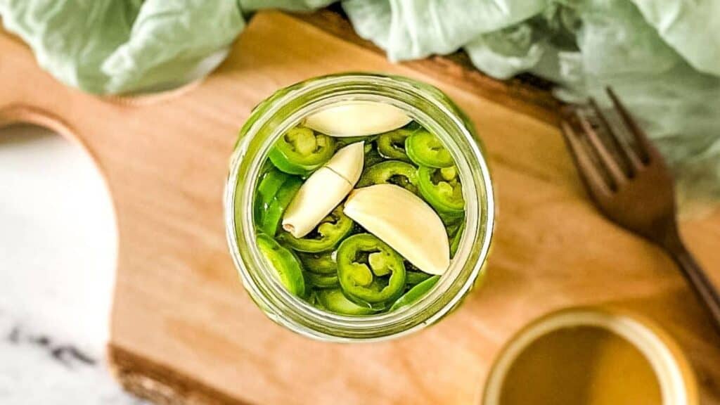 Pickled serrano peppers and garlic cloves in a glass jar.