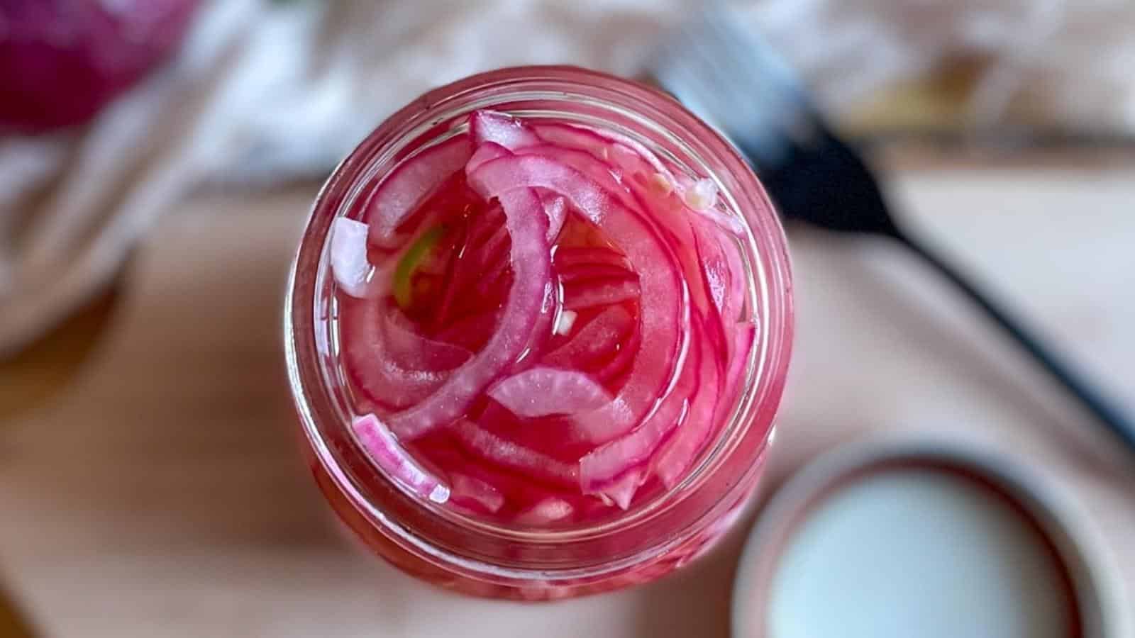 Overhead shot of spicy pickled onions in a glass jar.