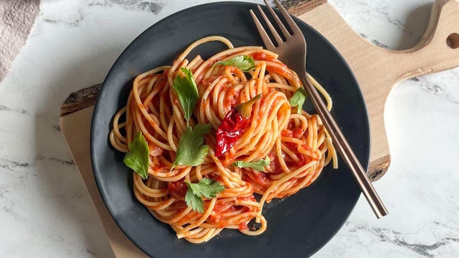 Spaghetti Arrabbiata is twirled on a black plate on a white marble counter.