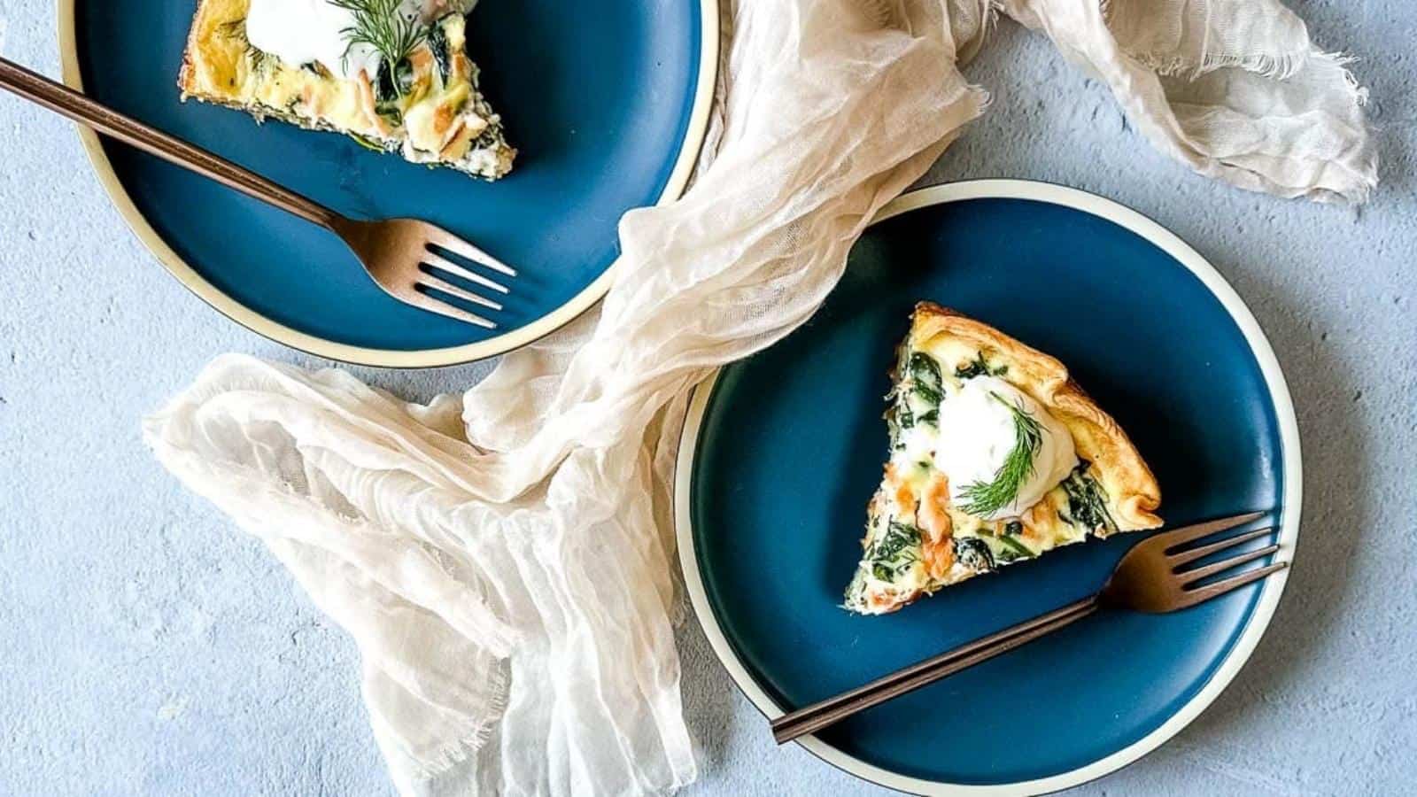 two slices of smoked salmon and spinach quiche on dark blue plates.