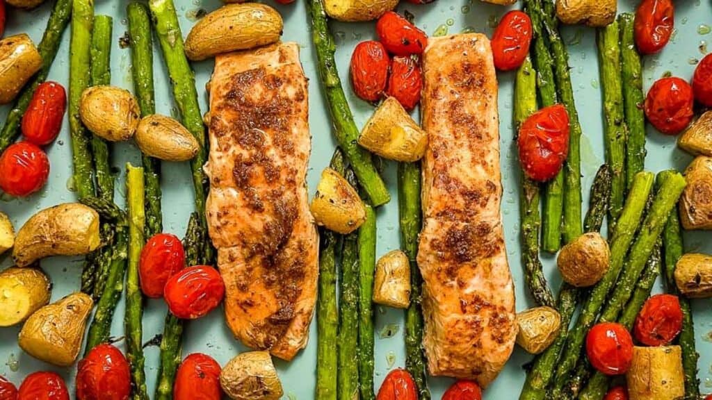 Salmon, asparagus, cherry tomatoes, and roasted fingerling potatoes on a blue sheet tray.
