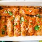 Chicken slow cooker enchiladas in a baking dish with two copper forks.