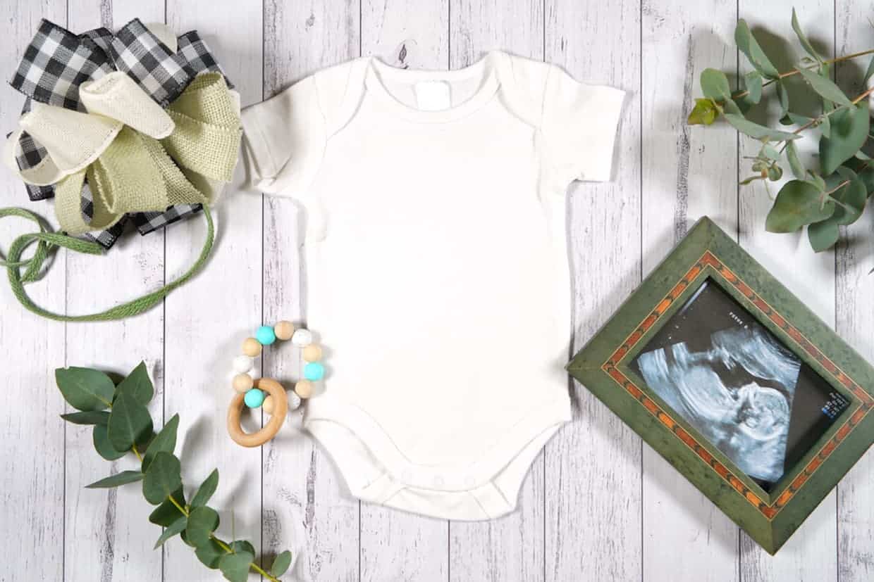 A flatlay of baby onesie and ultrasound as a cute idea on how to reveal pregnancy.