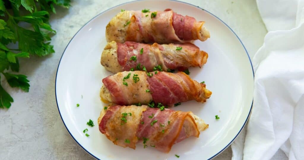 bacon wrapped chicken tenders on a white plate with parsley.