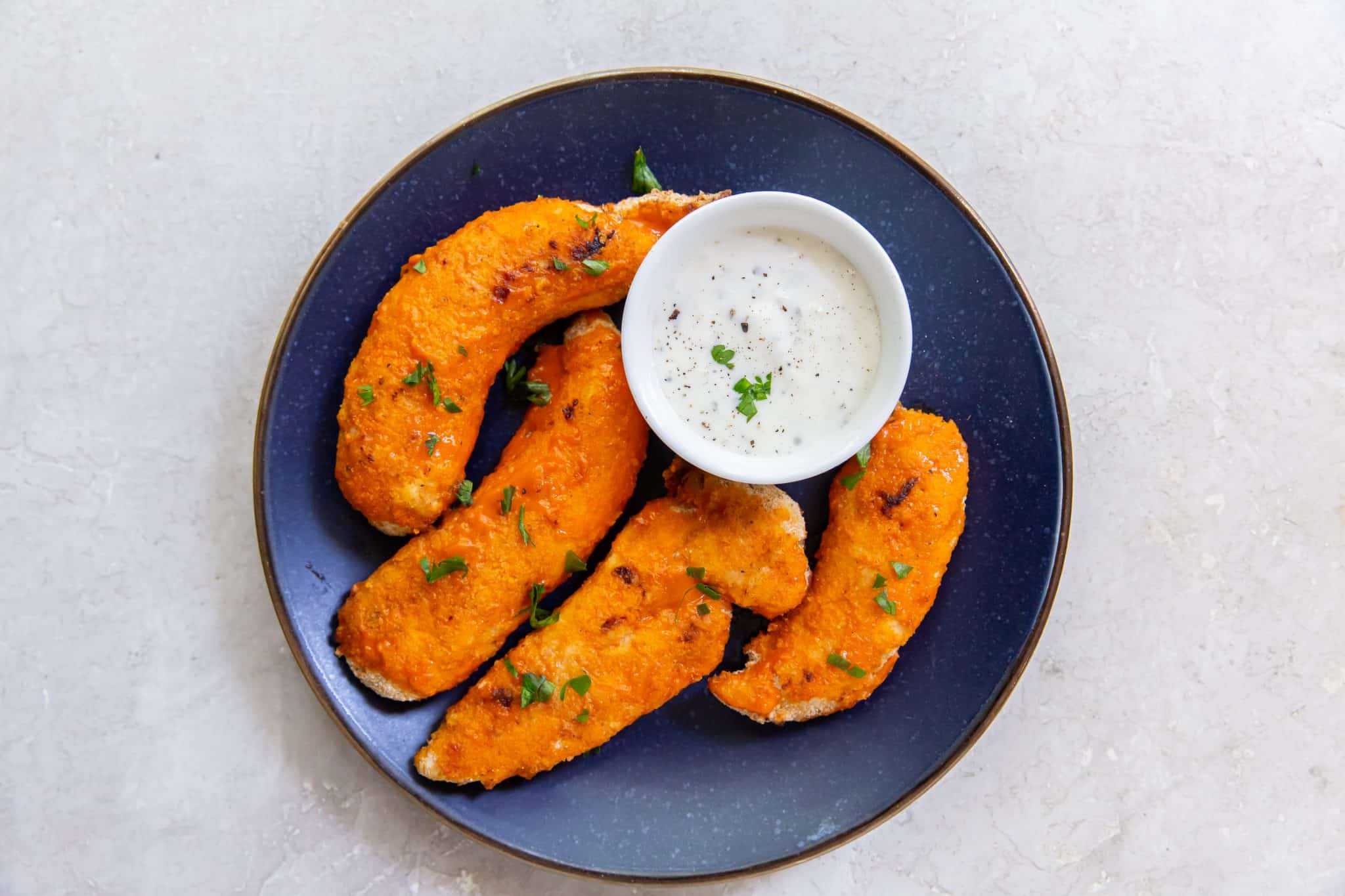 Easy Air Fryer Buffalo Chicken Tenders on a blue plate with white sauce and parsley.