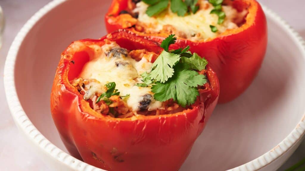 Two stuffed peppers in a bowl with melted cheese on top.
