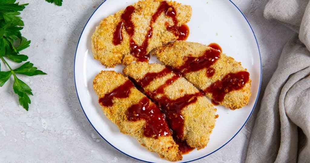 Air fryer katsu chicken tenders on a white plate with sauce.