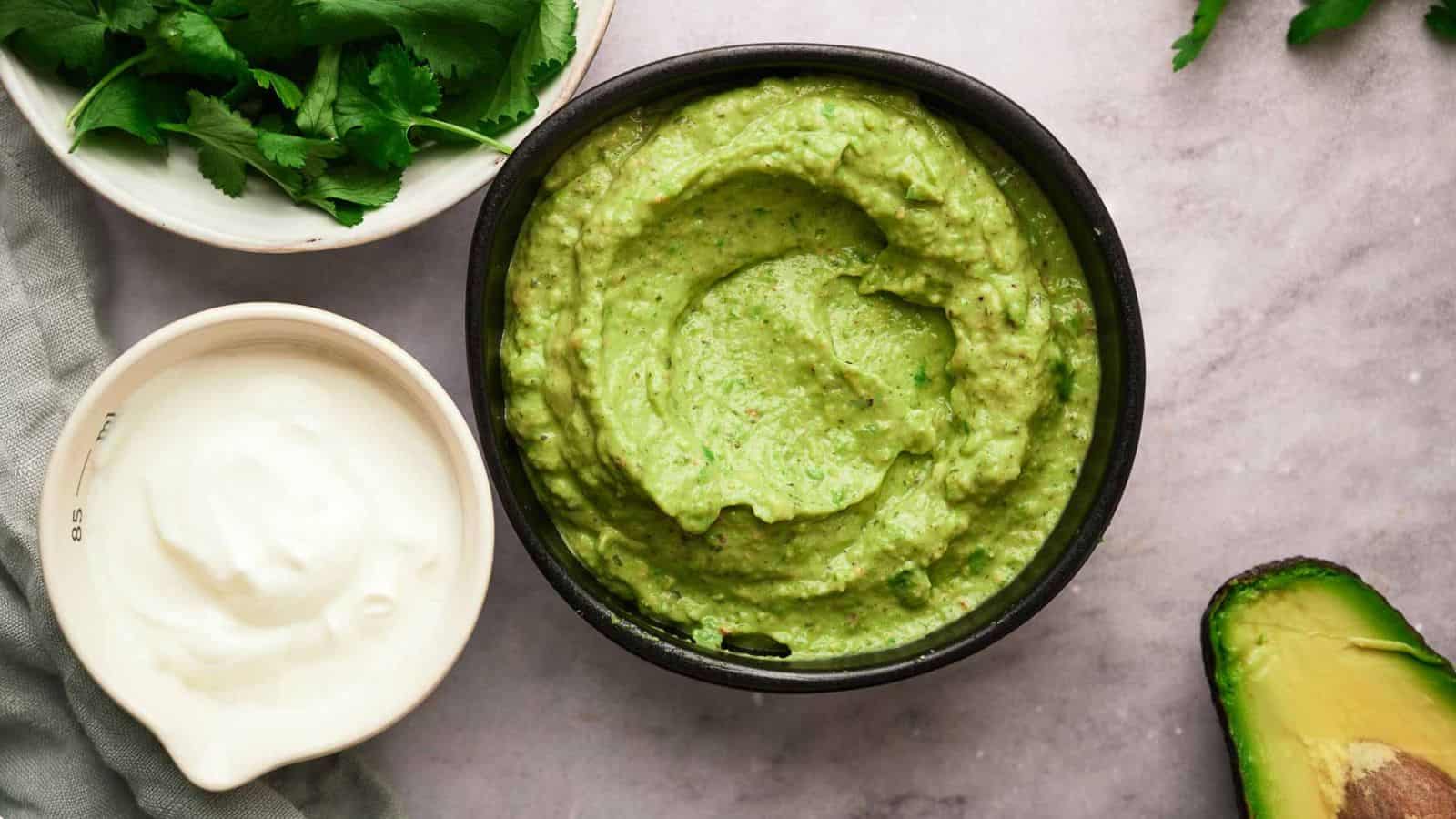 Avocado sauce in a bowl with it's ingredients surrounding it.