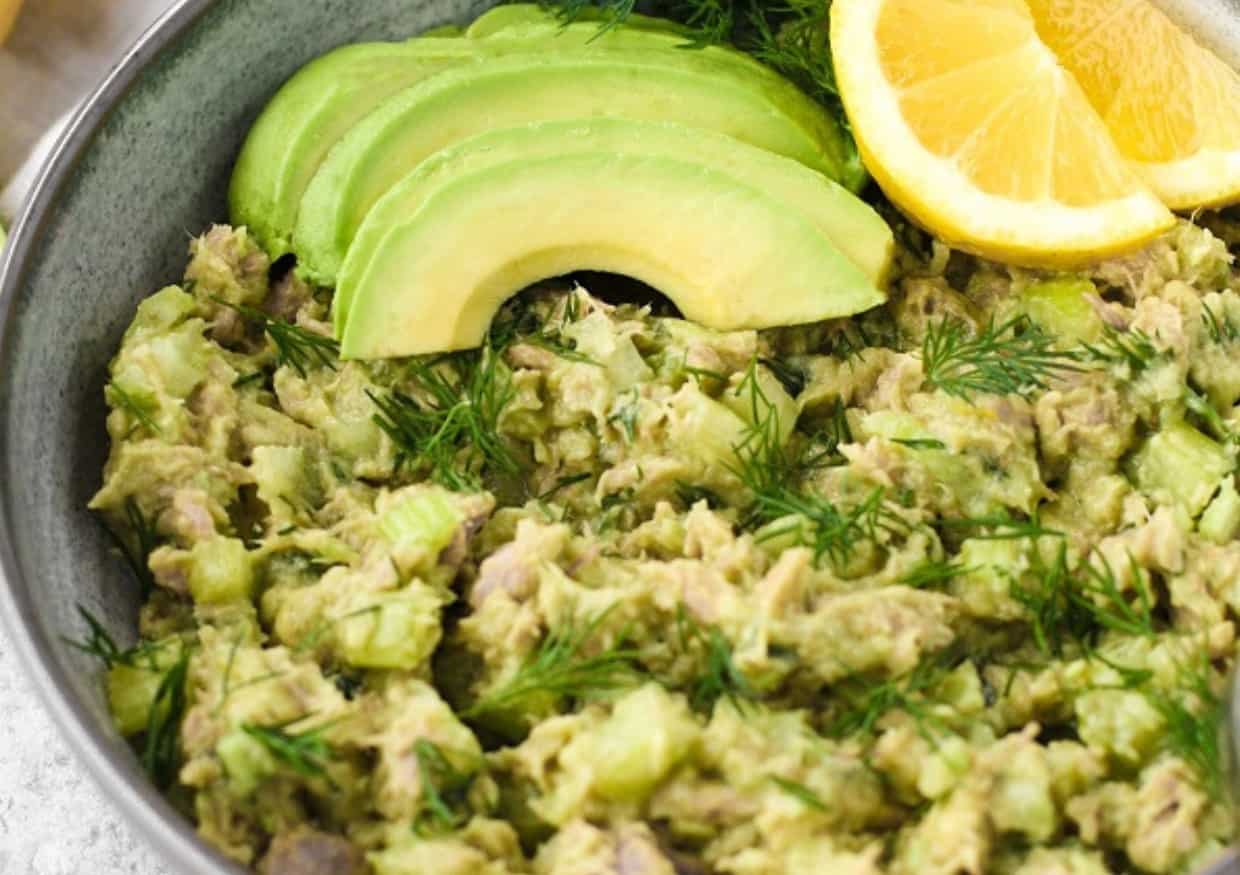 A bowl of avocado tuna salad with avocado slices and lemon slices.