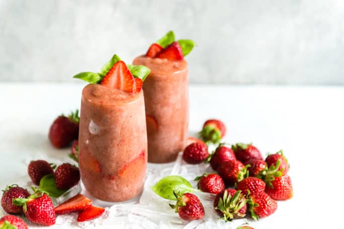 Pink frozen drink in tall glasses garnished with strawberries. 
