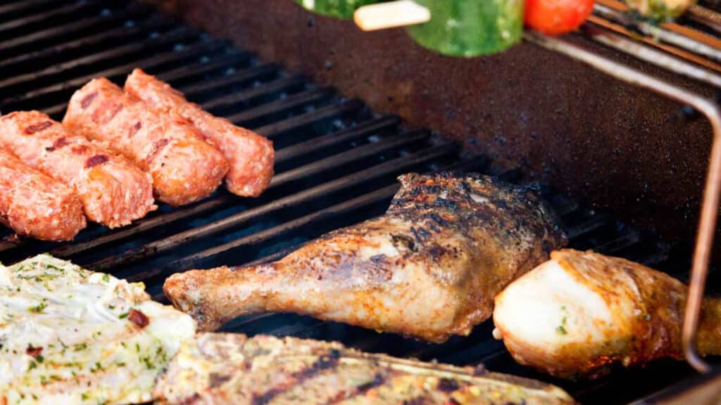 Chicken and beef are grilled beside vegetables skewers and sausages.