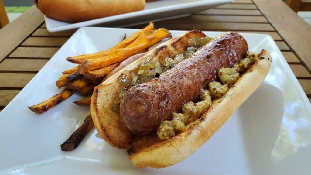 Beer boiled brat on a white plate with fries.