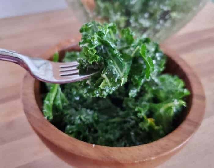 Image shows a fork holding a bite of lemon kale salad with the full bowl behind it.