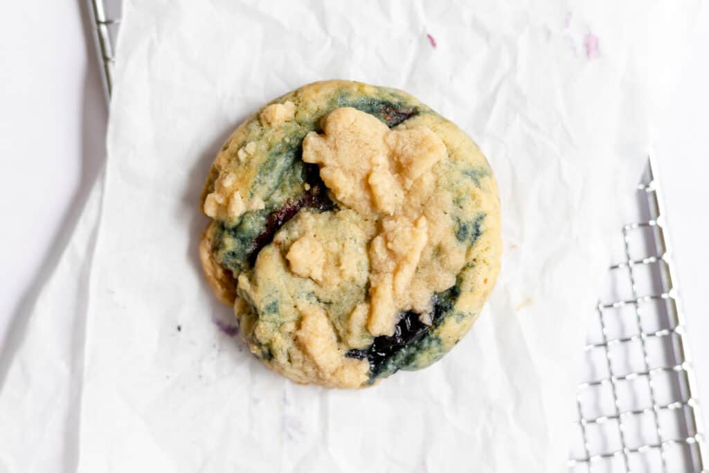 One fresh blueberry cookie on parchment paper over small baking rack. 