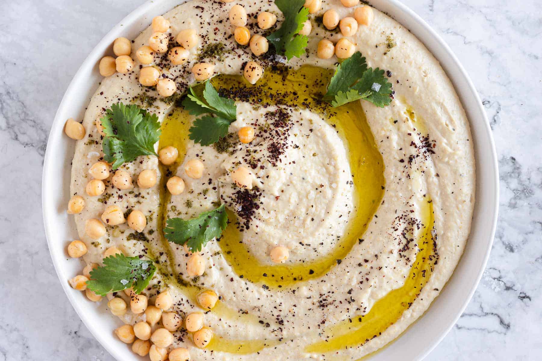 Garlic hummus on plate with parsley, zaatar and olive oil.