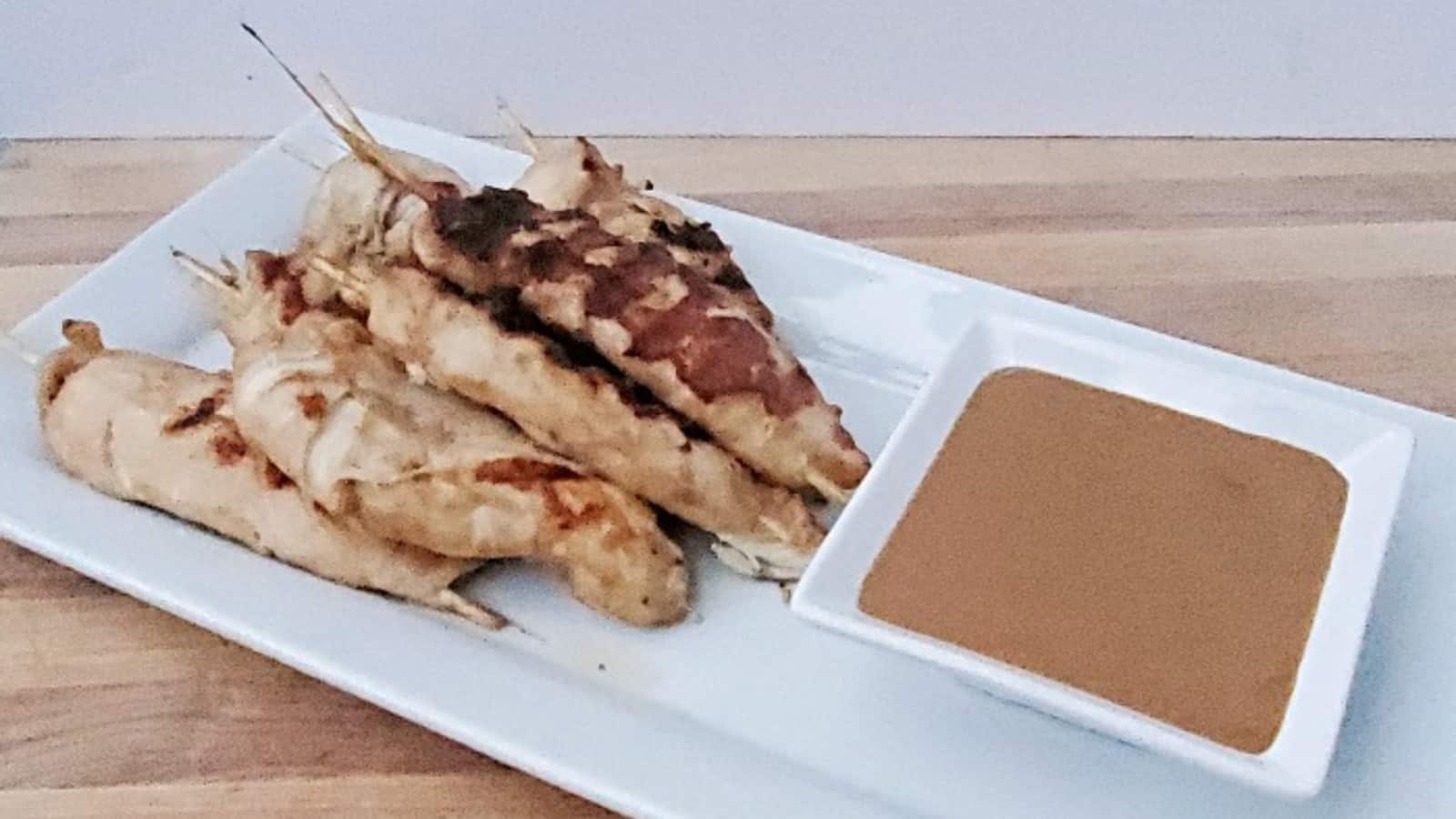Chicken satay with peanut sauce on a white platter.