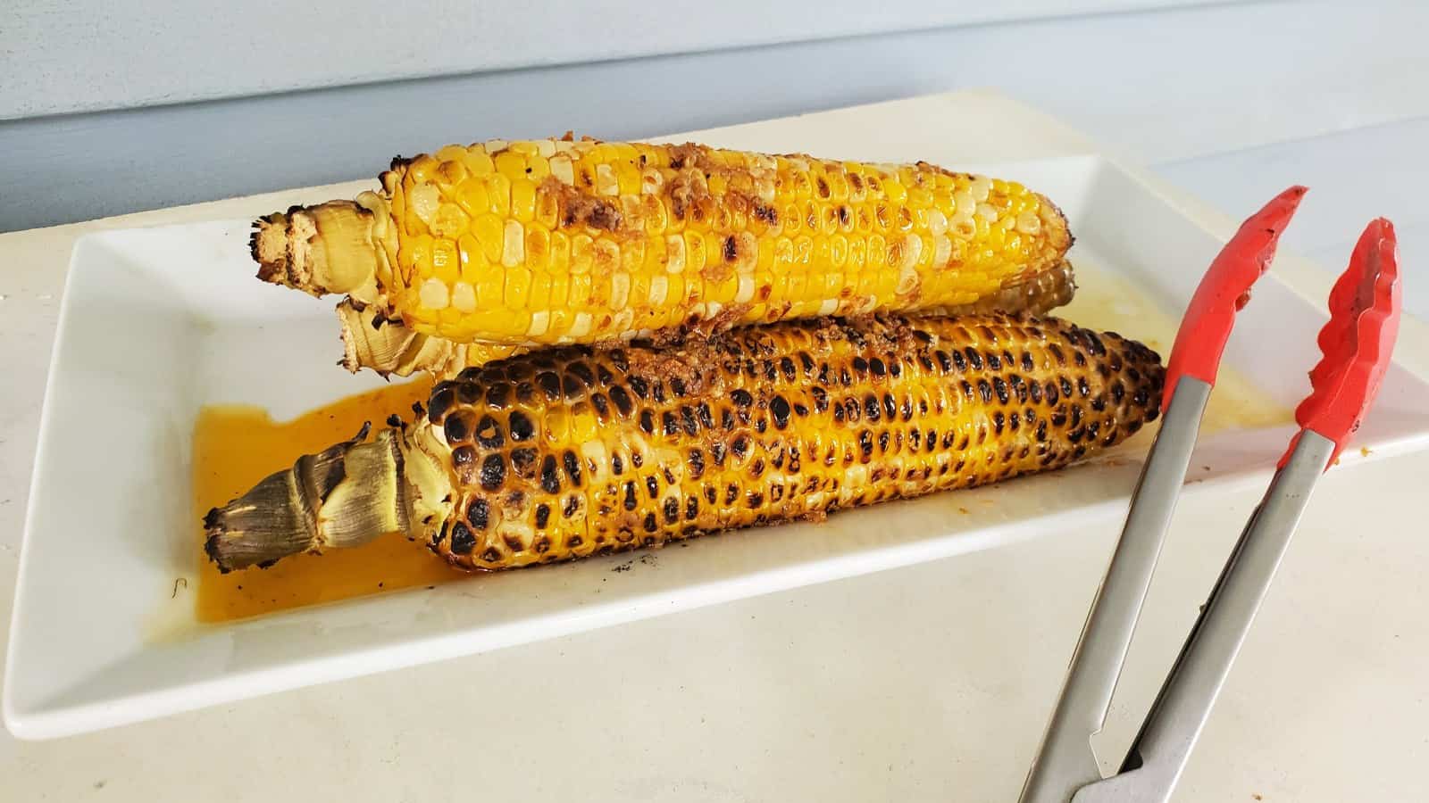 Image shows a white tray filled with chipotle grilled corn on the cob sitting on green grass.