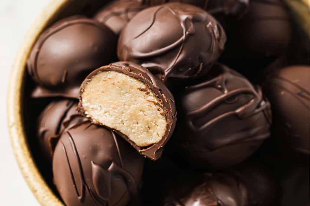 A bowl of chocolate-covered peanut butter balls with one cut in half.