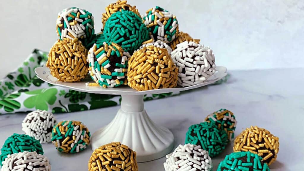 Green, gold and white sprinkle covered truffles on a white pedestal.