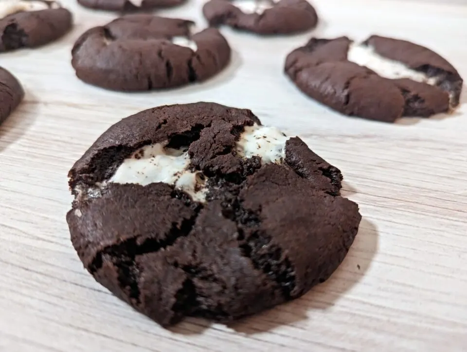 Image shows a series of chewy s'mores cookies on a wooden board.