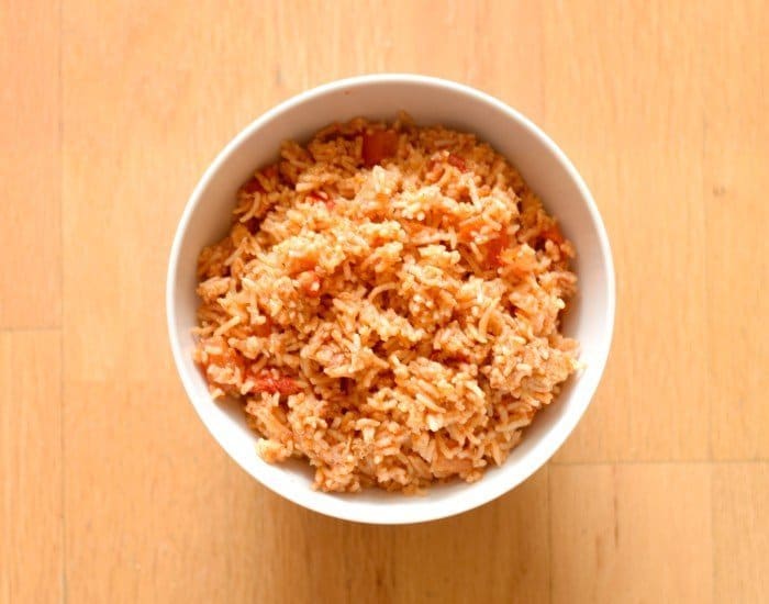 Overhead image of a white bowl containing Spanish rice sitting on a wooden board.