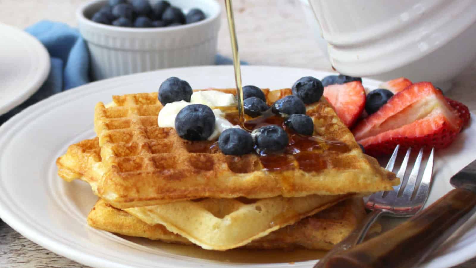 A stack of waffles with fruit and pouring syrup.
