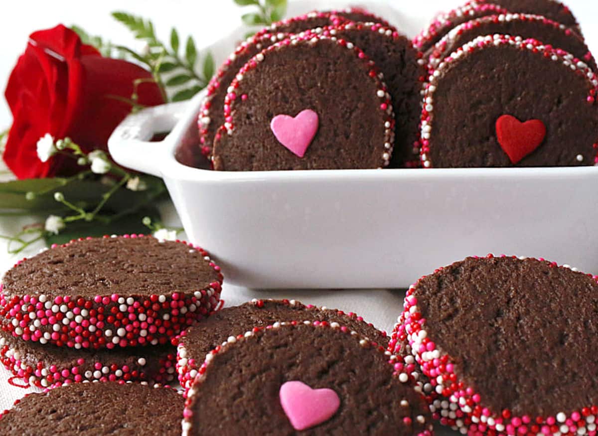 Chocolate shortbread cookies with sprinkles on the edges in a white dish.