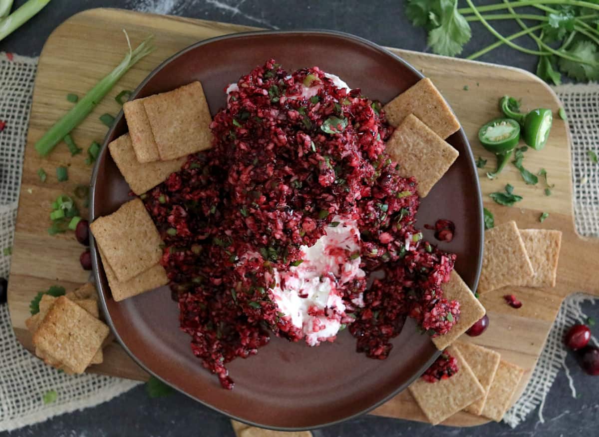 A brown plate with cranberry salsa and  cream cheese with crackers.