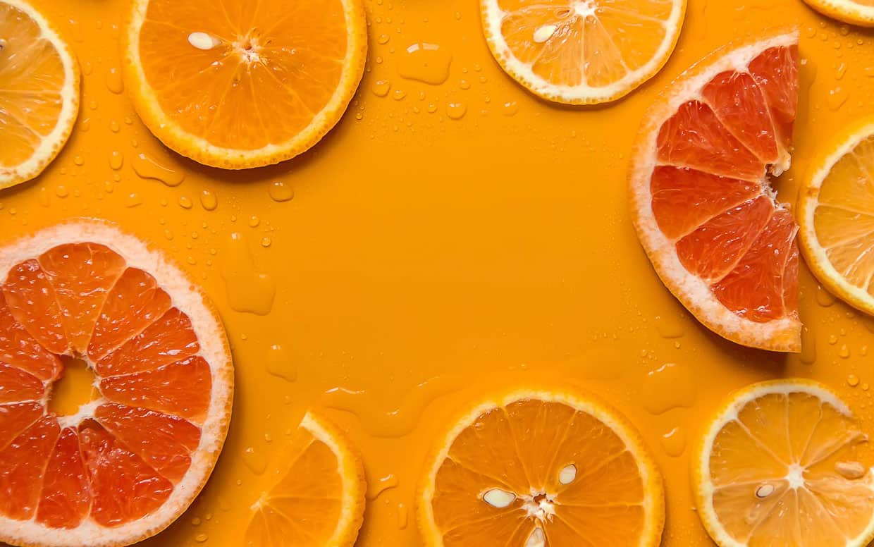 Sliced citrus fruits on an orange background.