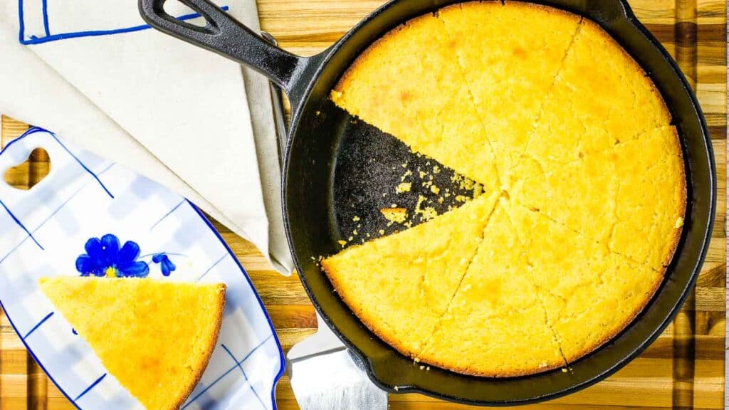 Overhead shot of cornbread in a cast iron skillet with a single slice cut out. 