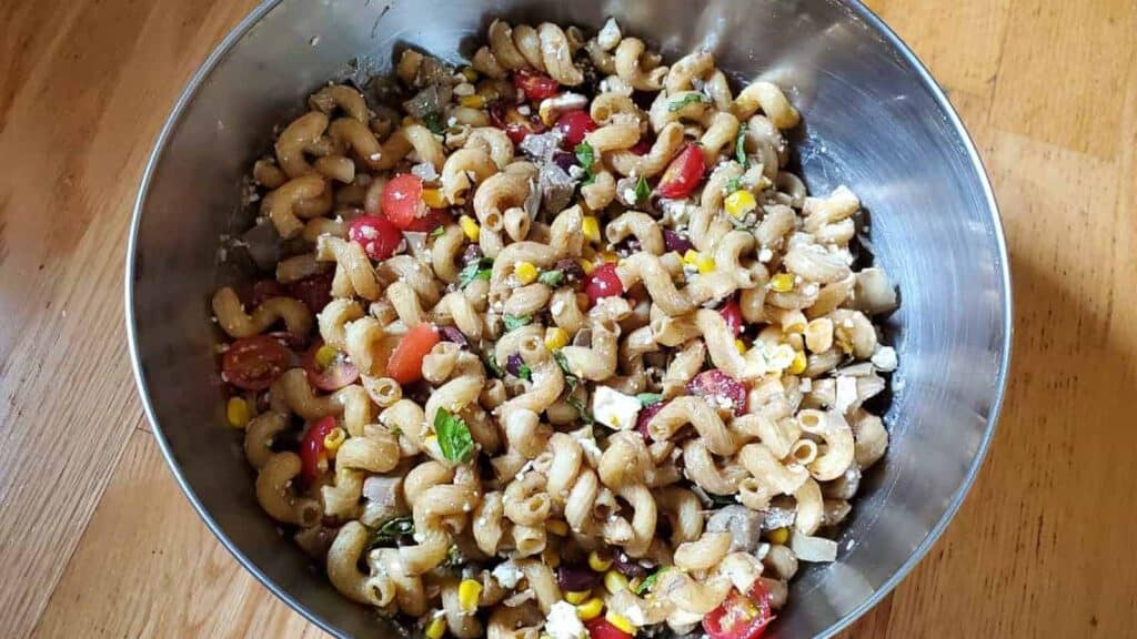 Overhead shot of Greek vegetable pasta salad in a silver bowl.