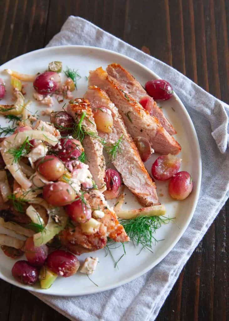 Grilled pork chops sliced on a plate with grapes and fennel.