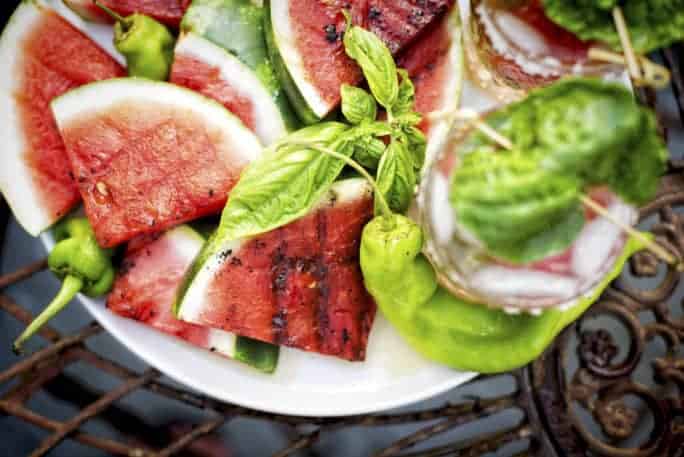 Overhead shot of platter of grilled watermelon with cocktails in soft focus.