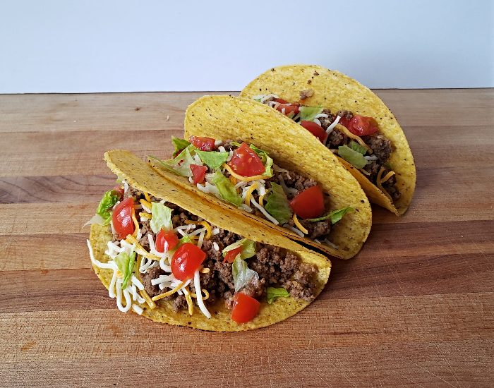 Image shows three honey habanero tacos with corn shells sitting on a wooden board.