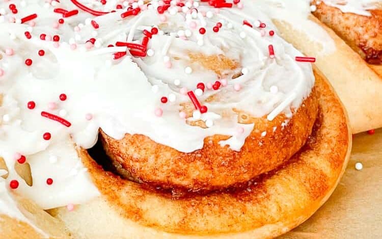 Cinnamon roll heart with white frosting and sprinkles. 