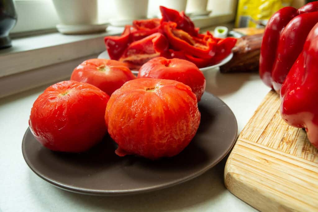 Peeled tomatoes on a plate with other vegetables around them.