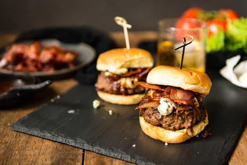 Two burgers with bacon and blue cheese on top.