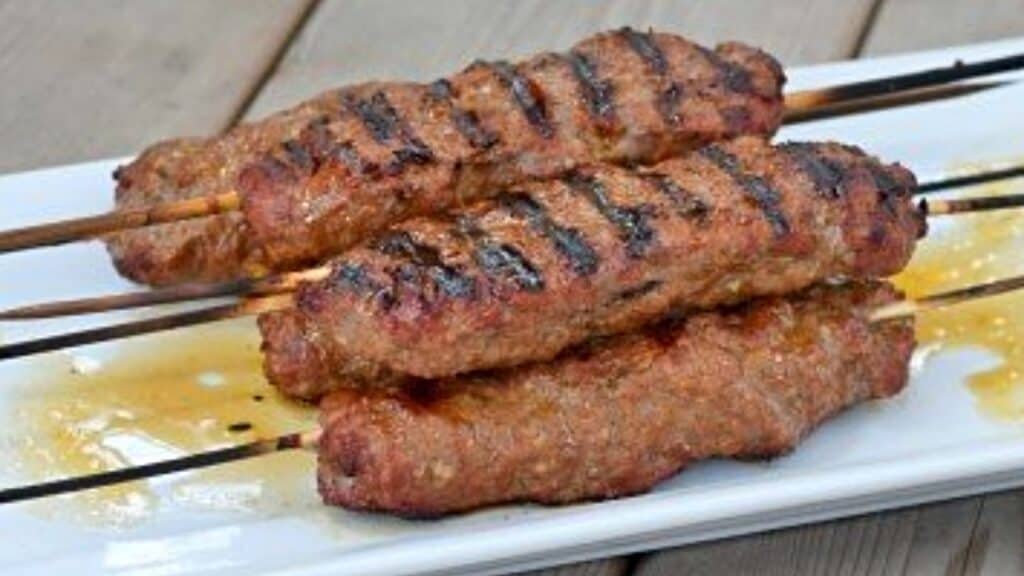 Kefta kebabs on skewers on a white platter.