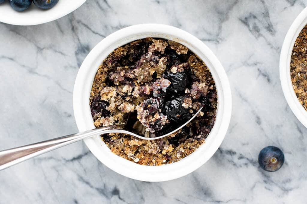 A ramekin of keto blueberry crumble with a spoon in it.