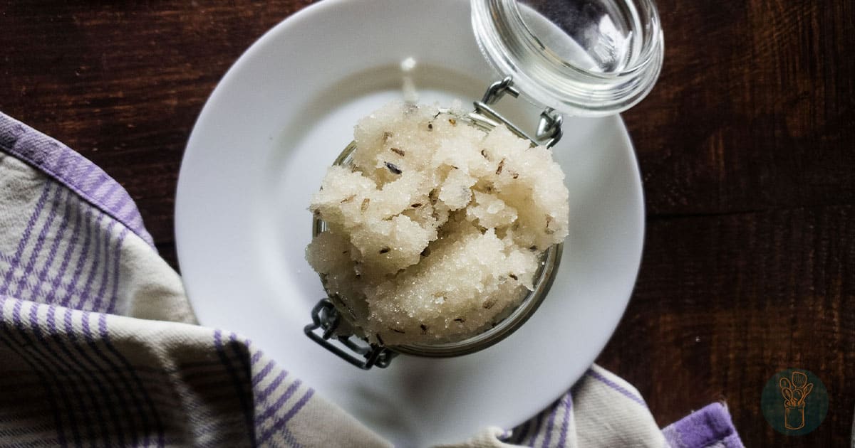 Lavender sugar scrub recipe in jar with lid on white plate with wooden table. 