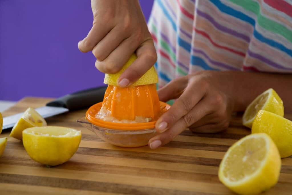 Woman preparing lemon juice with juicer on violet background.