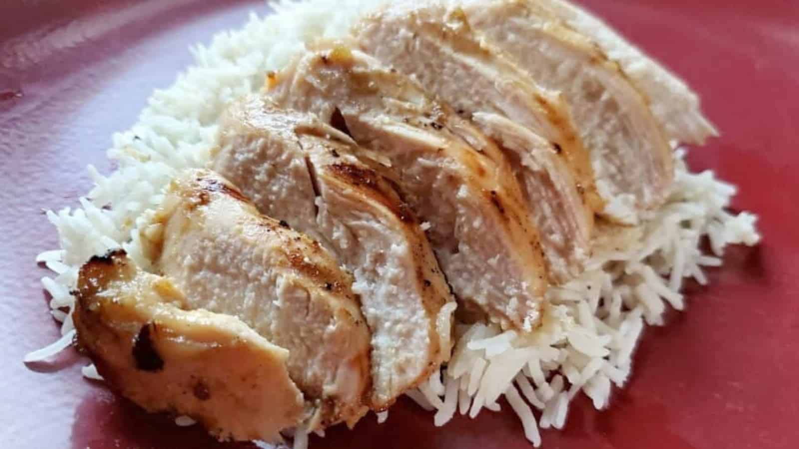 Lime marinated grilled chicken sliced on a red plate over rice.