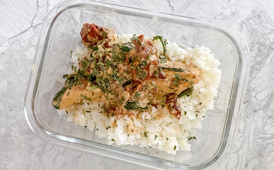 Meal prep Tuscan chicken and cauliflower rice in a glass container.