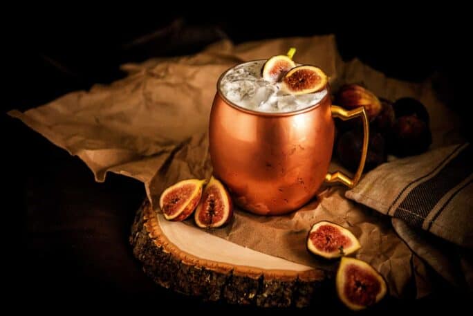 Dark photo of copper moscow cup filled with muddled figs and liquid.