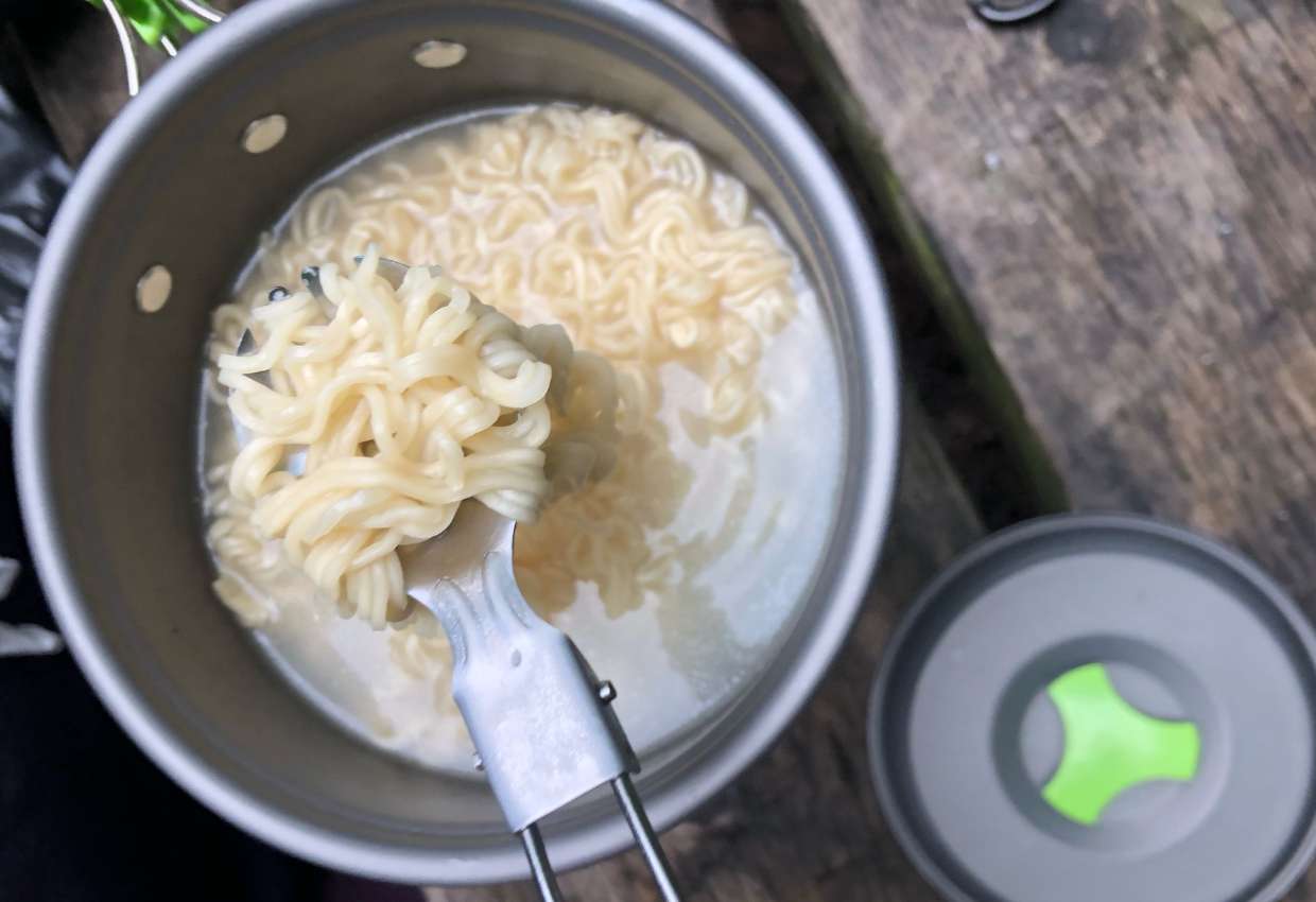 Mult-use spoon with noodles in pot on picnic table.