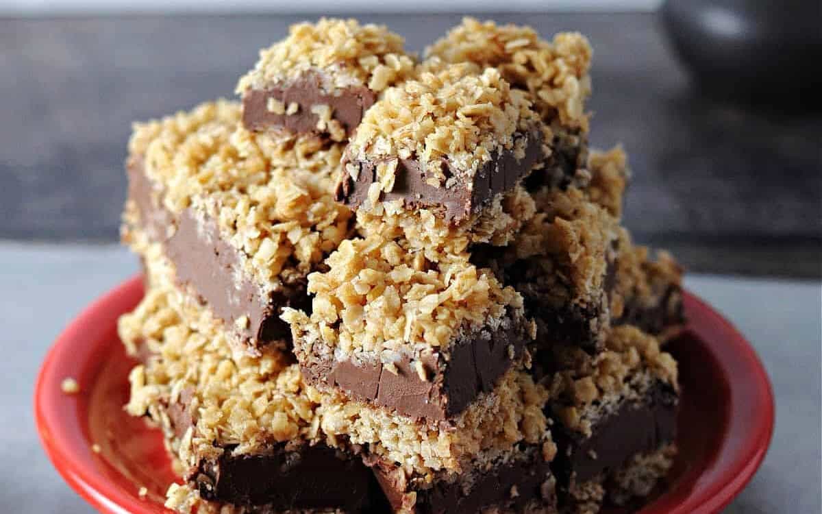 Red plate with chocolate peanut butter oatmeal bars squares stacked.