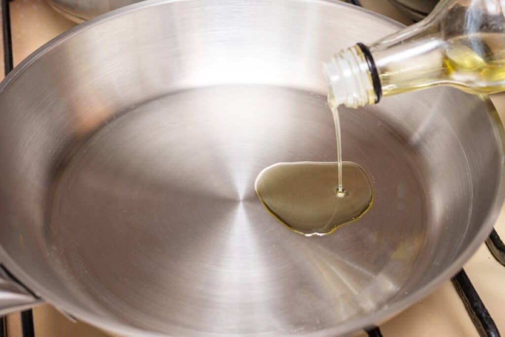 Olive oil being poured into a stainless steel pan.